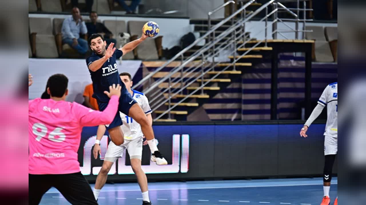 لقطة من مباراة كرة يد يظهر فيها لاعب يسدد بالكرة أمام حارس مرمى ومدافعين