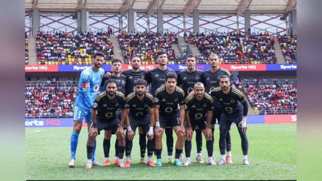 صورة جماعية للاعبي فريق يرتدون قمصاناً سوداء في صفين على أرض الملعب، وحارس يقف إلى جانبهم بقميص أزرق، وخلفهم مدرجات ممتلئة بالجماهير.