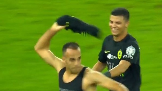لاعب يرفع قميصًا أسود داخل الملعب بينما يقف لاعب آخر خلفه.